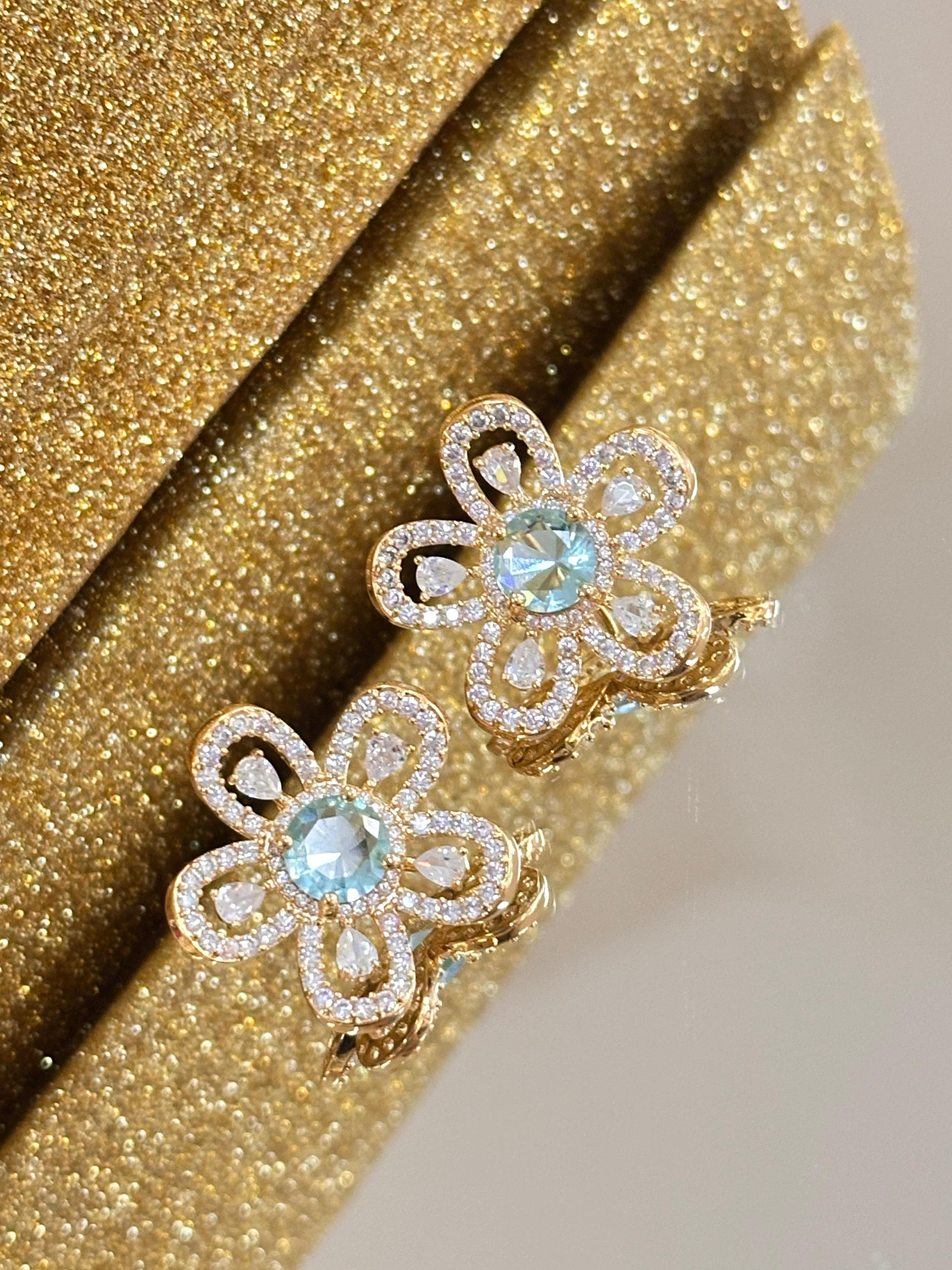Brinco floral dourado cravejado com zircônia azul no centro