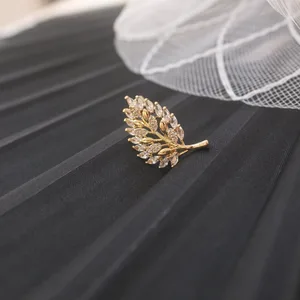 Broche dourado em formato de folha cravejada de cristais