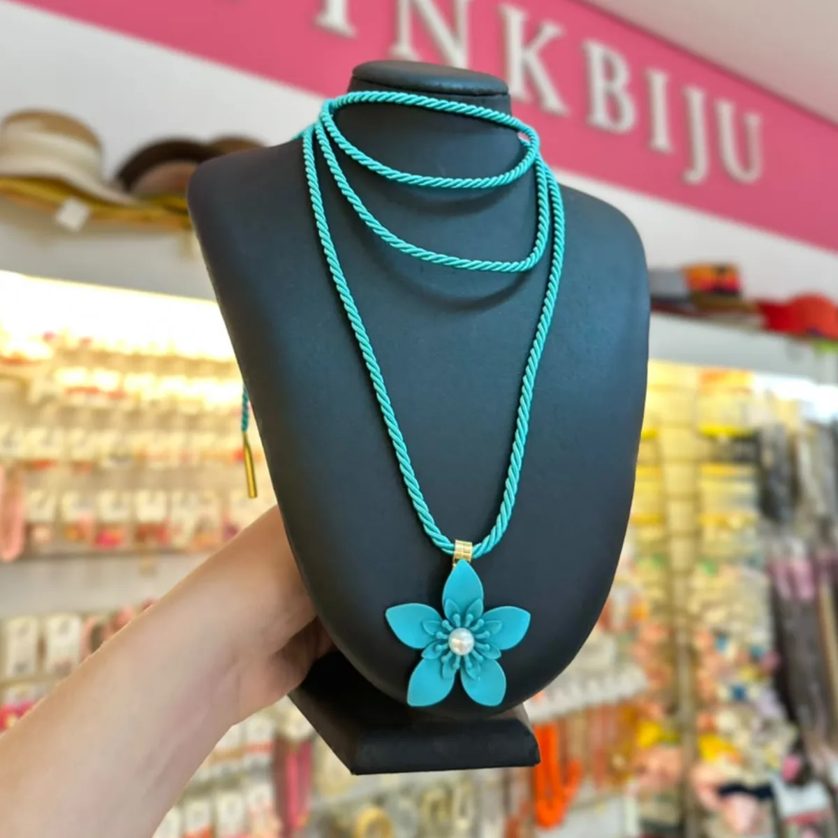 Colar de cordão torcido turquesa com pingente de flor e pérola, no busto preto da loja PinkBiju