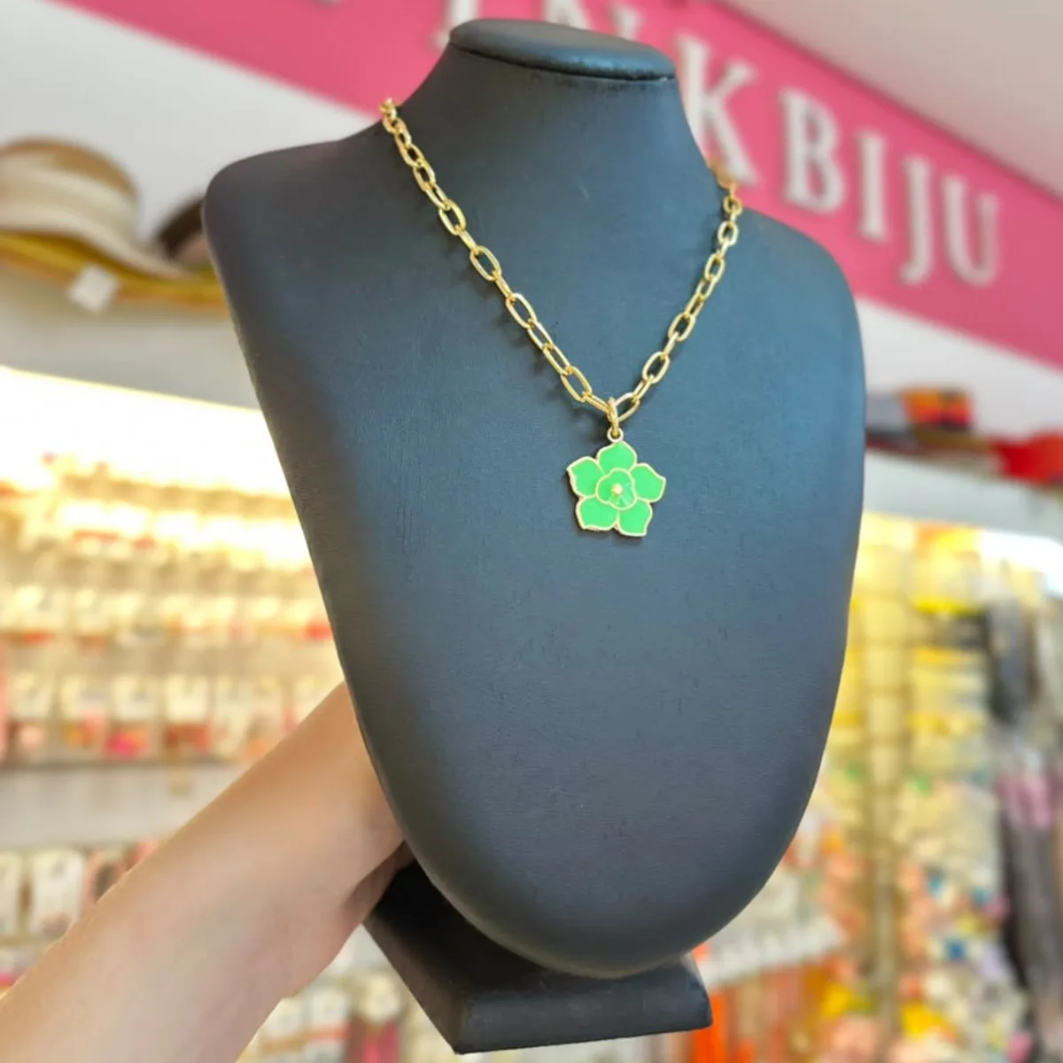 Colar de corrente dourada de elos com pingente de flor verde, no busto preto da loja PinkBiju