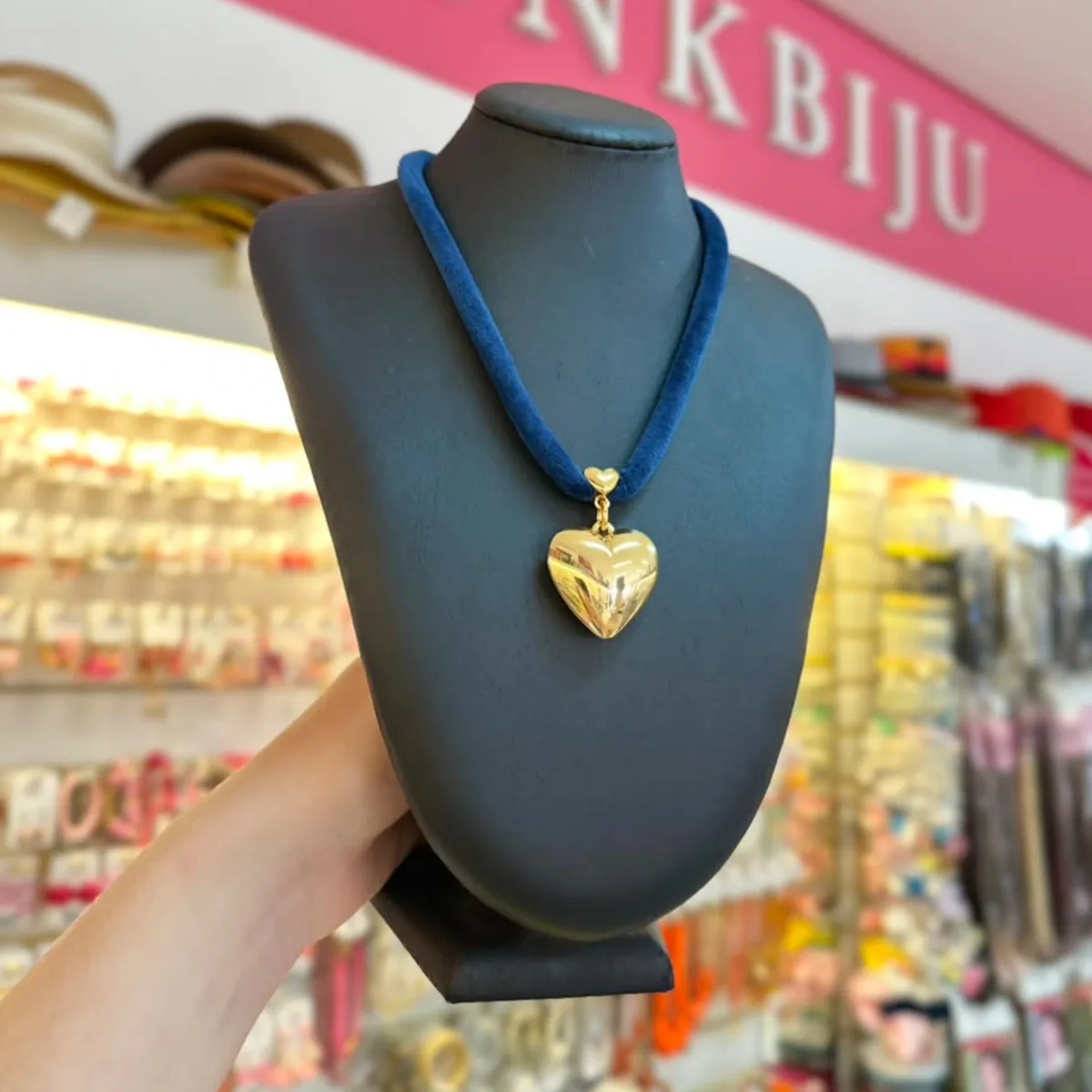 Colar de veludo azul com pingente de coração dourado, no busto preto da loja PinkBiju